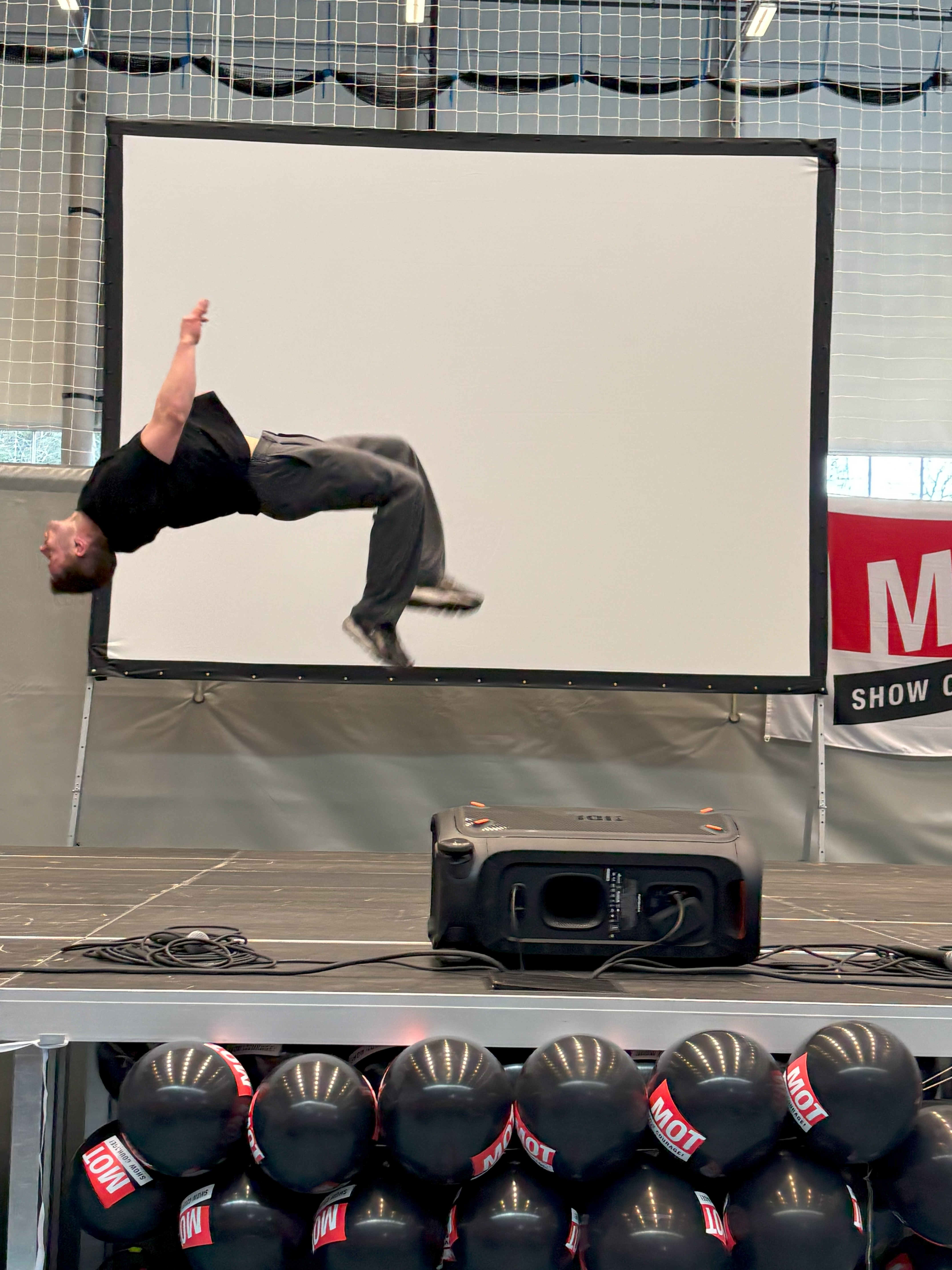 en person som gjør en flip på en scene med en stor projektorskjerm